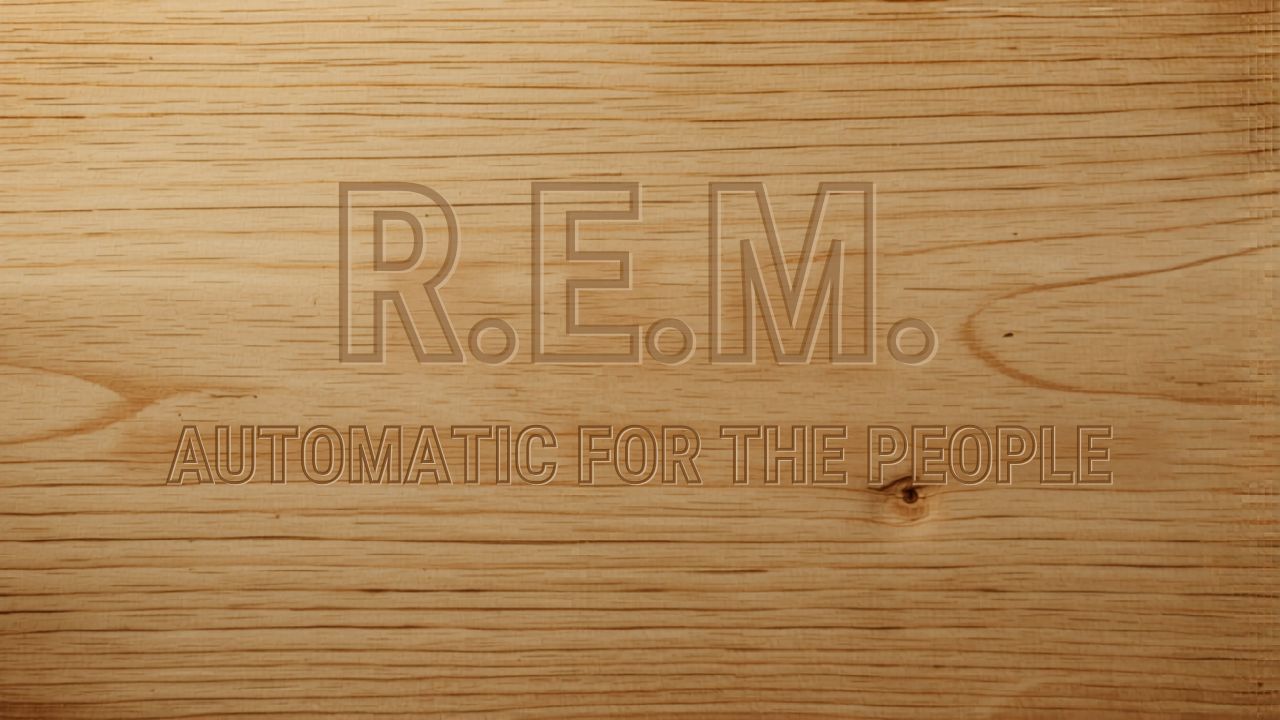 A close-up of warm pale wood grain, with "R.E.M." and "AUTOMATIC FOR THE PEOPLE" pressed into the surface as if carved there. The kind of thing you might find on a shelf, slightly forgotten, until you need it.