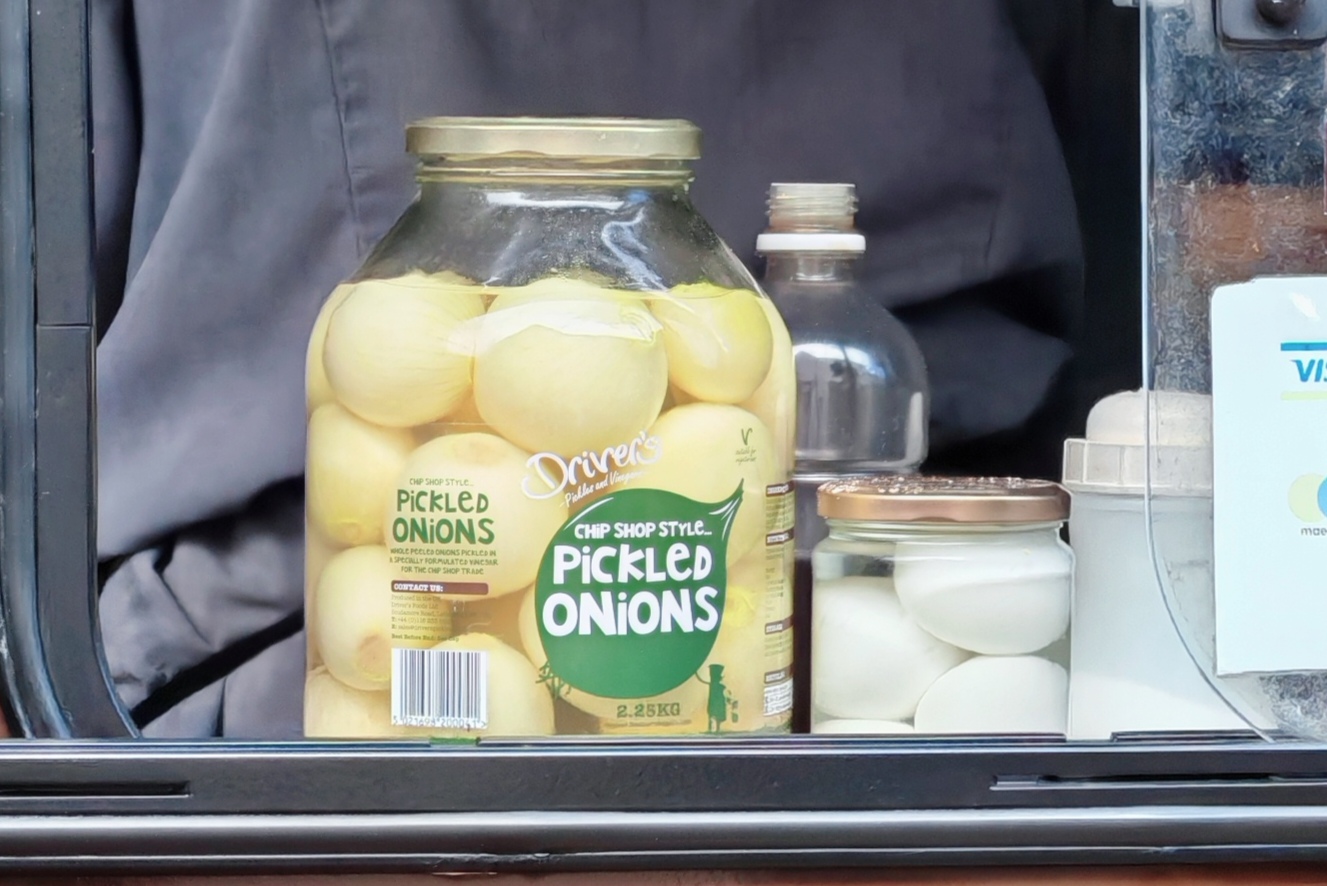 Photo: Large glass jar of Driver's "Chip Shop Style Pickled Onions" (2.25kg) sitting in the window of a chip shop van, surrounded by other condiment containers. The industrial-sized jar suggests serious pickled onion consumption is expected.