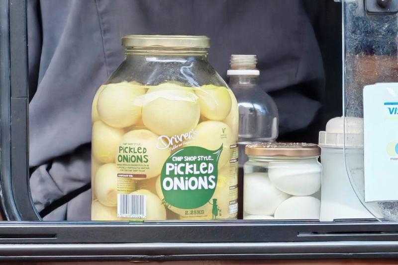 Photo: Large glass jar of Driver's "Chip Shop Style Pickled Onions" (2.25kg) sitting in the window of a chip shop van, surrounded by other condiment containers. The industrial-sized jar suggests serious pickled onion consumption is expected.