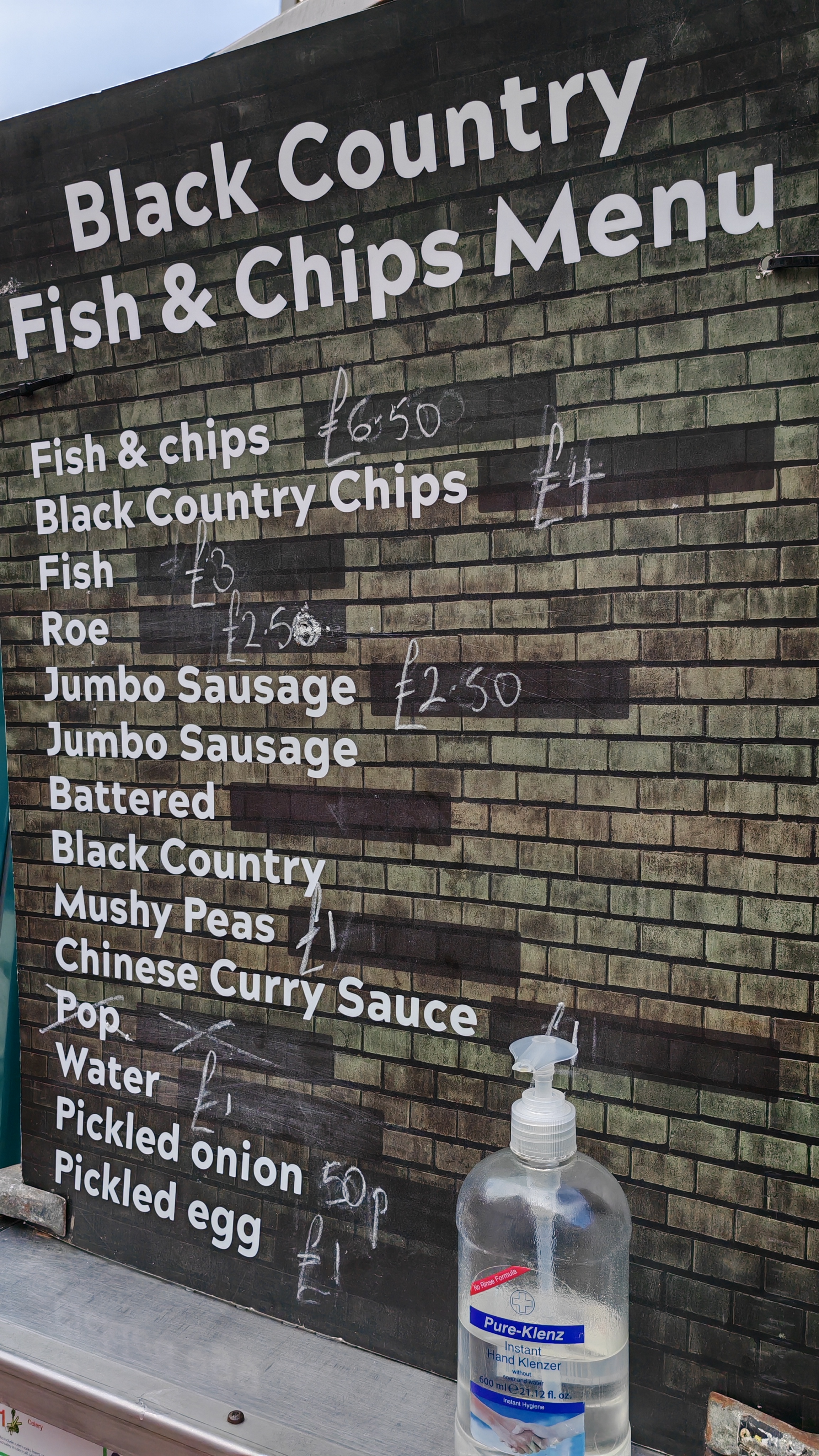 Photo: Chalk menu board for "Black Country Fish & Chips Menu" displaying prices including fish & chips (£6.50), various items like jumbo sausage (£2.50), and notably pickled onion (50p) and pickled egg (£1) at the bottom.