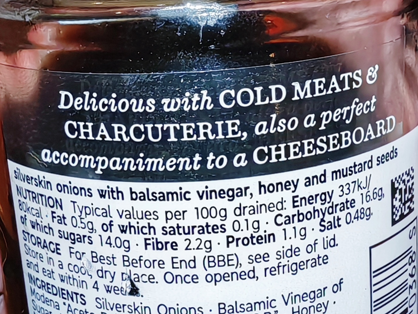 Close-up of a jar label for M&S Collection Balsamic Pickled Onions, showing the product description "Delicious with COLD MEATS & CHARCUTERIE, also a perfect accompaniment to a CHEESEBOARD" along with nutritional information and ingredients list including silverskin onions with balsamic vinegar, honey and mustard seeds.