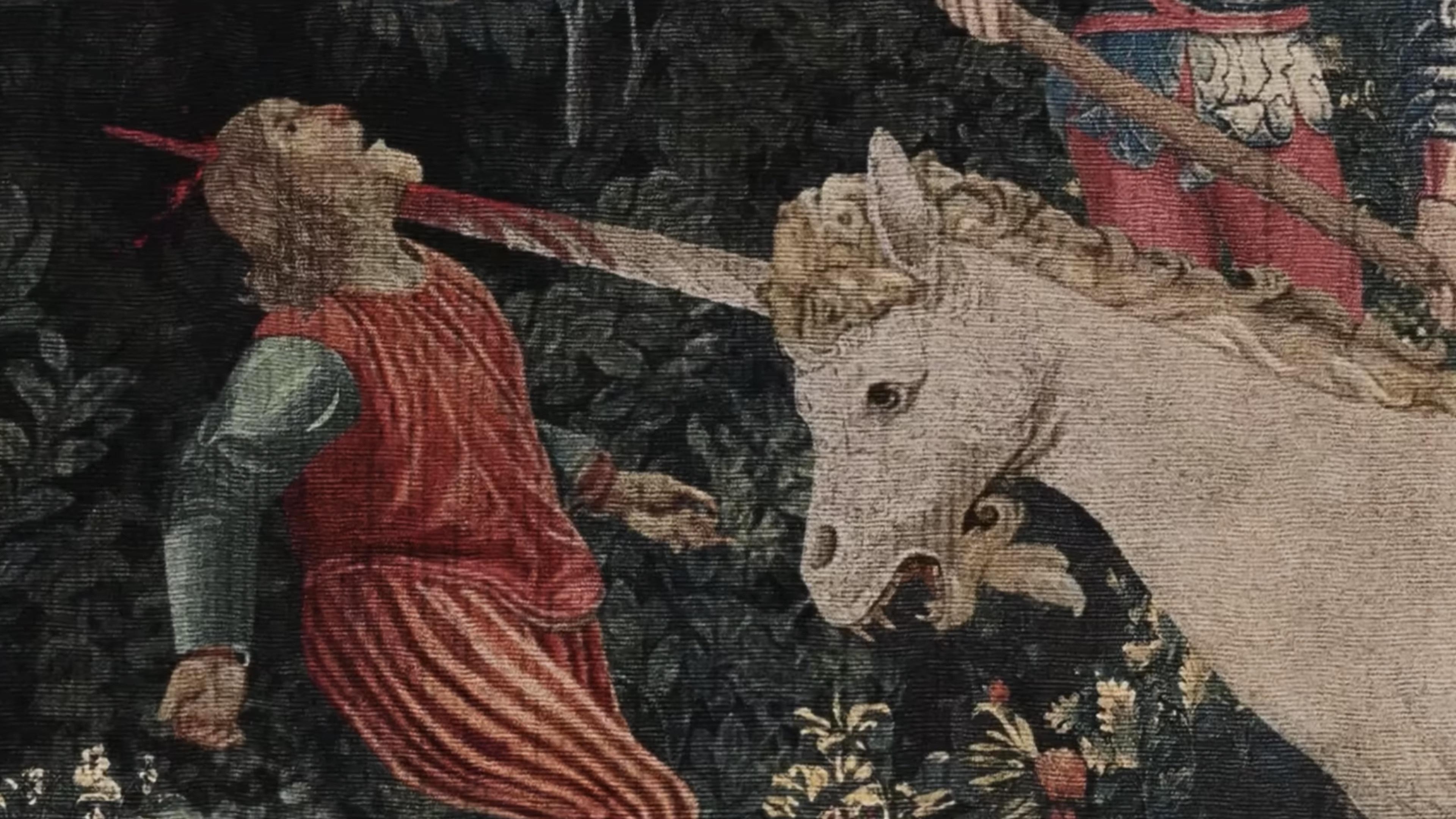 Film still showing a medieval tapestry depicting a peasant in flowing red robes who has been impaled by a white unicorn's horn, which is now stained with blood. The scene is set against a dark floral background in the style of classic medieval tapestries. Well, that's certainly put a dampener on all those romantic unicorn myths - turns out the pointy bit wasn't just for show after all.