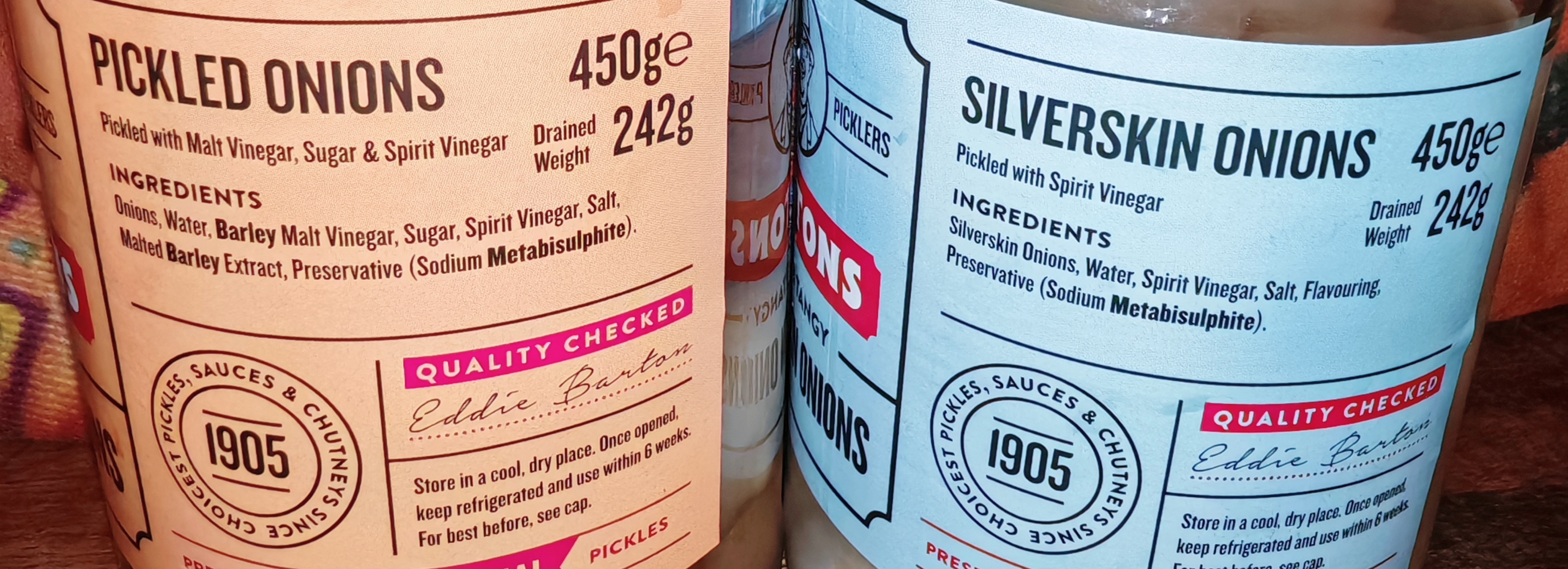 Close-up of jar labels showing ingredients. Traditional Pickled Onions (beige label) lists ingredients: Onions, Water, Barley Malt Vinegar, Sugar, Spirit Vinegar, Salt, Malted Barley Extract, Preservative. Silverskin Onions (pale blue label) lists: Silverskin Onions, Water, Spirit Vinegar, Salt, Flavouring, Preservative. Both show "1905" heritage badge, "Quality Checked" stamp, and Eddie Barton 
