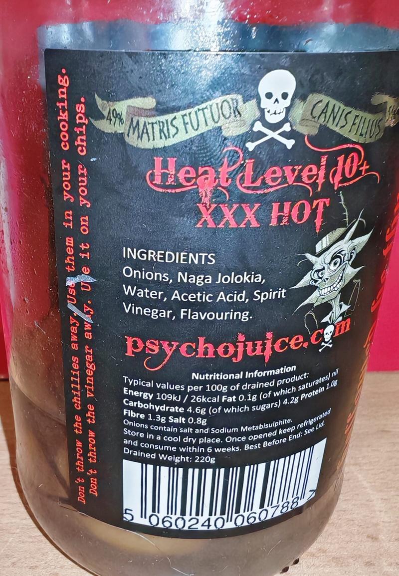 Photo: Ingredients and nutritional information panel showing "Heat Level 10+ XXX HOT." Lists ingredients as Onions, Naga Jolokia, Water, Acetic Acid, Spirit Vinegar, Flavouring. Includes standard nutritional values per 100g, storage instructions, and barcode. Website psychojuice.com visible.