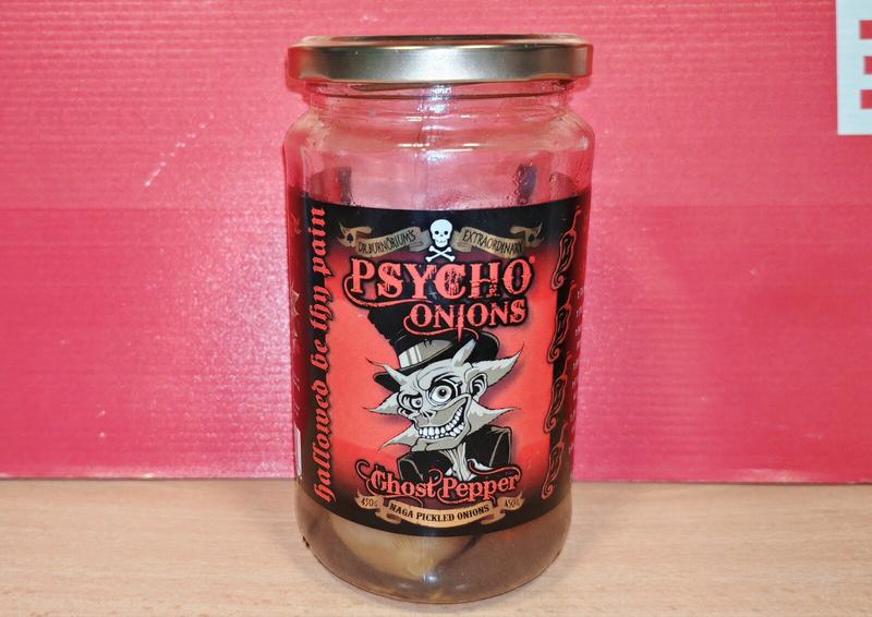 Photo: Glass jar of Dr. Burnorium's Extraordinary Psycho Onions Ghost Pepper Naga pickled onions on a red background. The label features a cartoon skull wearing a top hat with a manic grin, and red text on black. The jar contains pale onions in vinegar with a silver twist-off lid.