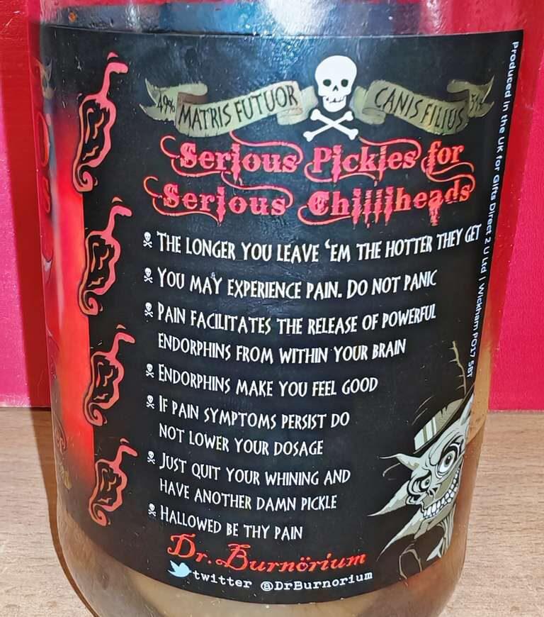 Photo: Close-up of jar label showing humorous warning text in white on black background. Header reads 'Serious Pickles for Serious Chilli heads' with skull and crossbones. Eight warning points include 'The longer you leave 'em the hotter they get,' 'You may experience pain. Do not panic,' and 'Just quit your whining and have another damn pickle.' Dr. Burnorium Twitter handle visible at bottom.