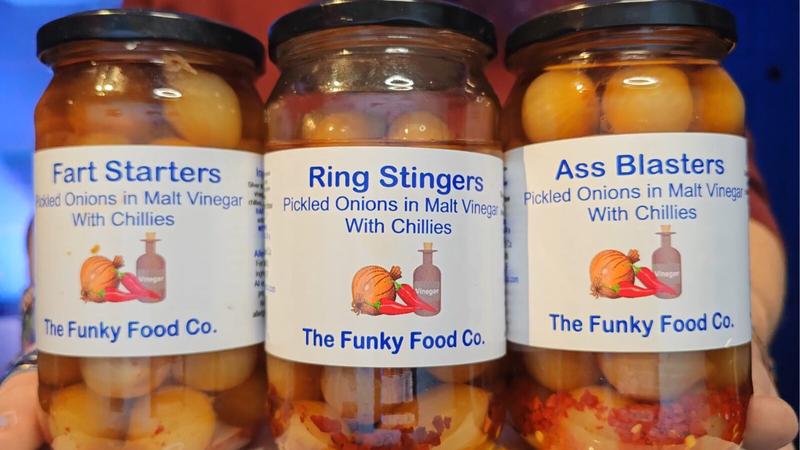 Photo: Three glass jars of pickled onions from The Funky Food Co. arranged left to right. Labels read "Fart Starters", "Ring Stingers", and "Ass Blasters" - all pickled onions in malt vinegar with chillies. Each label features an illustration of an onion, chillies, and a vinegar bottle. The jars contain pale onions visible through the glass, with varying levels of visible chilli pieces in the brine.