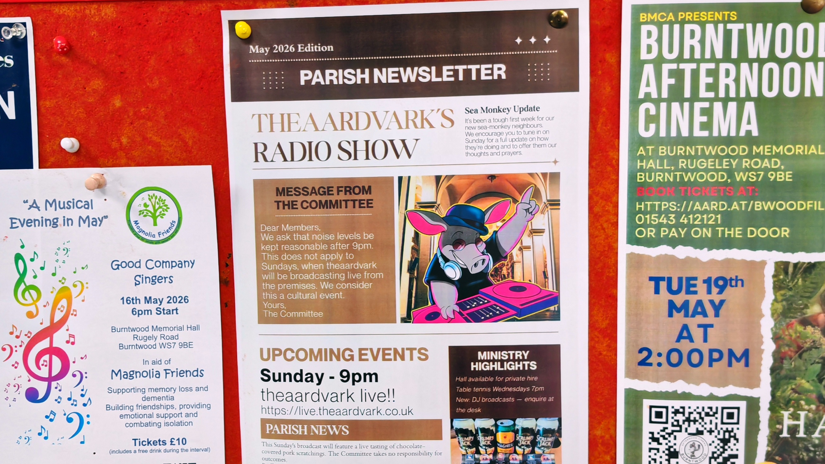 A printed parish newsletter titled "theaardvark's Radio Show," pinned to a community centre notice board. The newsletter promotes a Sunday 9pm live broadcast at live.theaardvark.co.uk, features a cartoon aardvark DJ, and includes a "Message from the Committee" asking members to keep noise levels down after 9pm — with an exception for Sundays, when theaardvark will be broadcasting live from the premises. To the left, a flyer for a Good Company Singers concert. To the right, a Burntwood Afternoon Cinema poster.