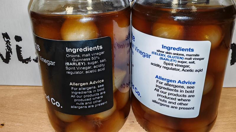 Close-up of the back labels of two Funky Food Co. jars showing ingredients and allergen information. The left jar (Guinness pickled onions) lists ingredients including onions, malt vinegar, Guinness 50%, barley, sugar, salt, spirit vinegar, acidity regulator, and acetic acid. The right jar (Marmite pickled onions) lists silver skin onions, marmite, celery, gluten, malt vinegar, barley, sugar, salt, spirit vinegar, acidity regulator, and acetic acid. Both labels include allergen advice highlighting ingredients in bold.