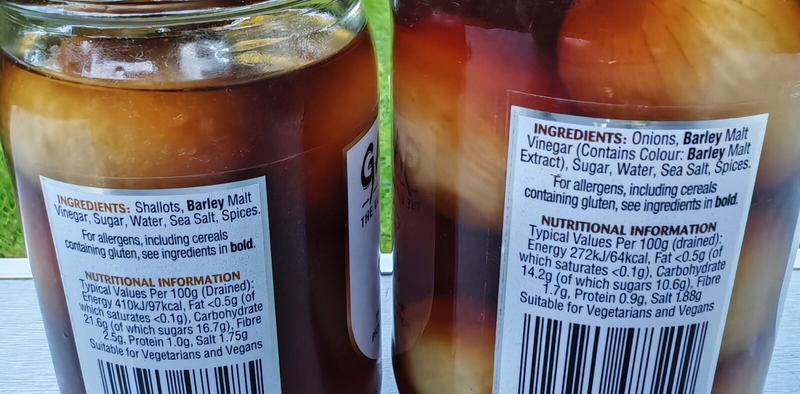 Photo: Close-up of the back labels of two Garner's jars showing ingredients and nutritional information. The left jar (Pickled Shallots) lists shallots, barley malt vinegar, sugar, water, sea salt, and spices. The right jar (Original Pickled Onions) lists onions, barley malt vinegar containing colour barley malt extract, sugar, water, sea salt, and spices. Both labels include allergen advice noting cereals containing gluten in bold, nutritional information per 100g drained, and confirmation that both products are suitable for vegetarians and vegans.