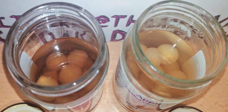 Top-down view looking into both opened jars. Left jar contains darker amber-coloured honey vinegar with pickled onions visible beneath the surface. Right jar shows lighter, clearer apple cider vinegar with pickled onions. Both jars show the liquid and onions from directly above.